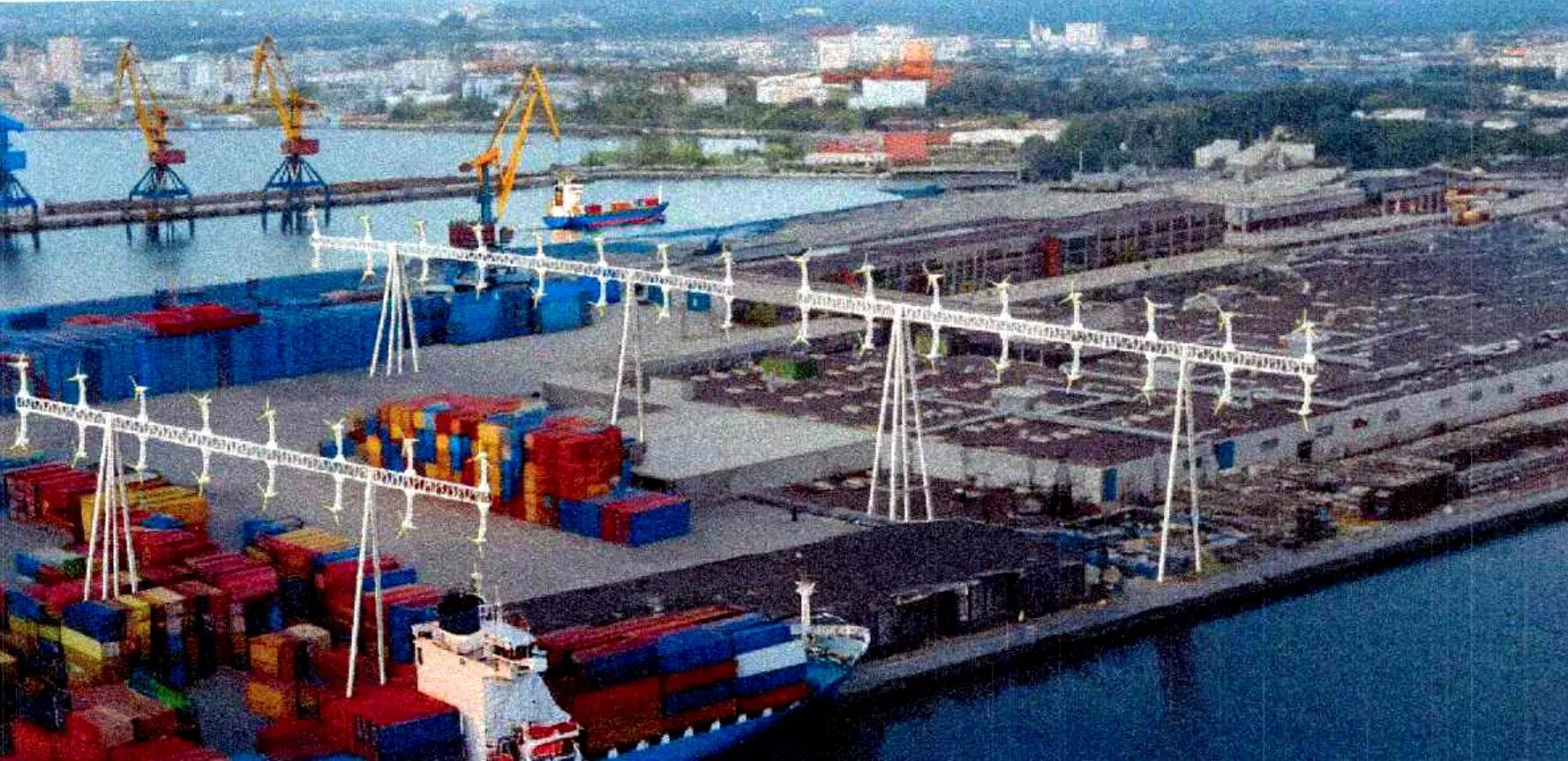 An aerial view of a container port with FlowGen turbine gantries spanning the stacks and the quay.
